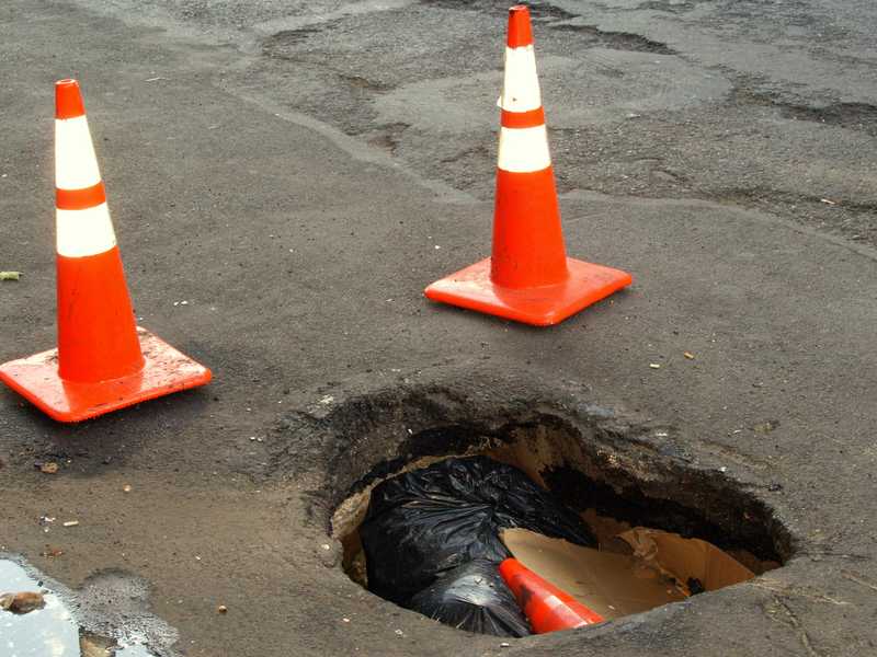 A deep pothole with a nearby patched area